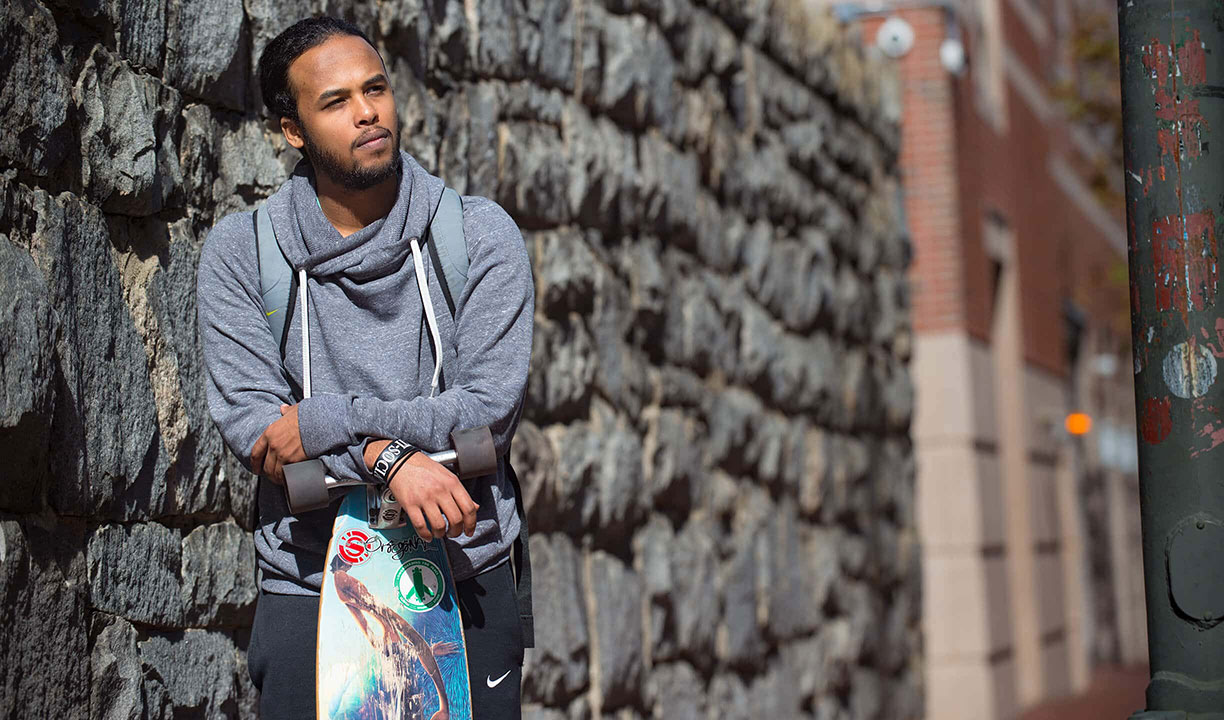 Male student stands in front of VCU building holding skateboard