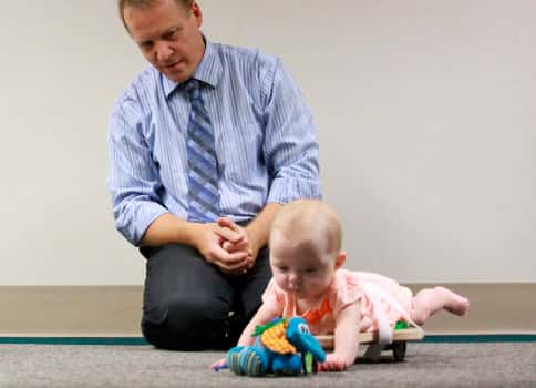 Researcher observing baby on skateboard-like device