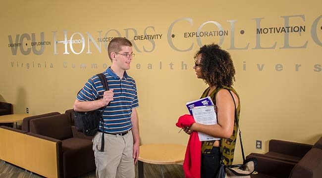 Two students talking in front of wall that says Honors College