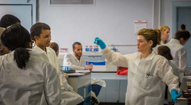 Student holding test tube in lab, surrounded by other students