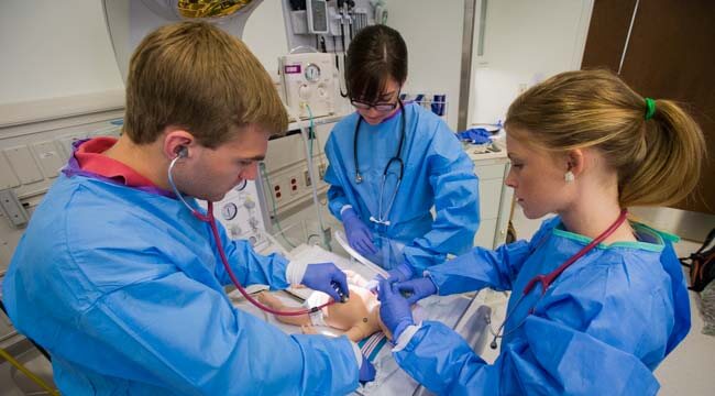 Students in scrubs working with baby mannequin 