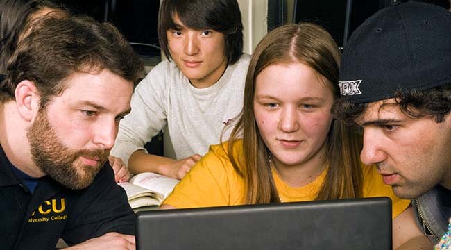 Four students clustered around laptop