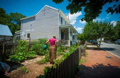 Woman watering plants in front of historic house