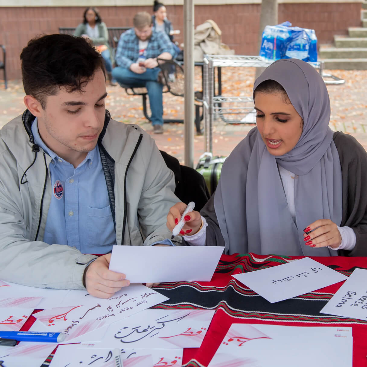 A student shows another student how to write in Arabic.